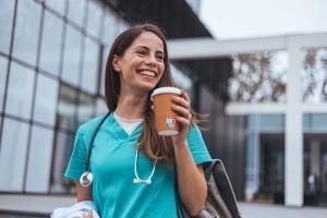 Smiling nurse holding a cup of coffee outside